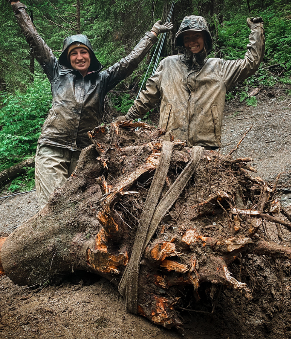 Two crew members pose in front of a large stump that was excavated from the trail.